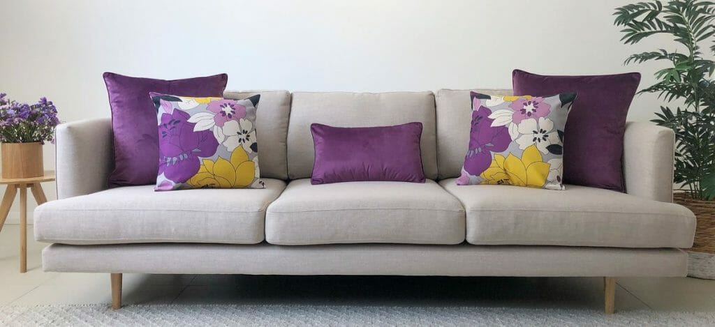 Purple floral and block coloured cushions in different sizes on a grey sofa.