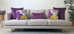 Purple floral and block coloured cushions in different sizes on a grey sofa.