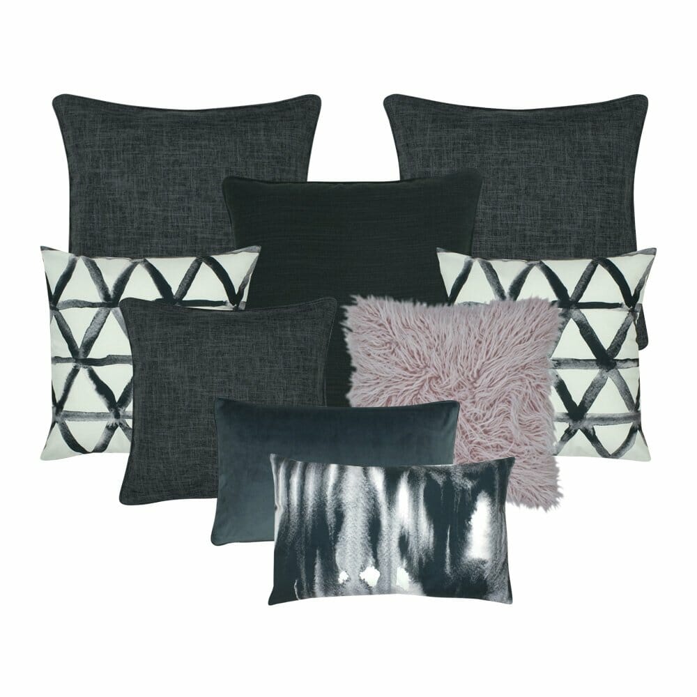 A lilac fur cushion with three plain grey cushion,a dark grey cushion, a pair of black and white patterned cushion and two rectangular cushion in shades of grey.