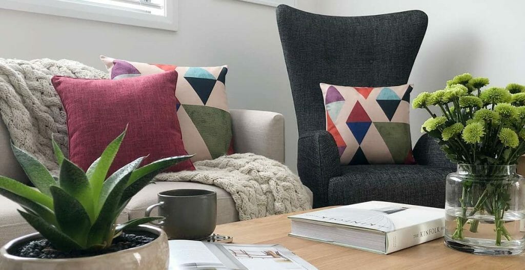 A cream sofa and dark grey high back chair decorated with colourful cushions for a pop of colour.