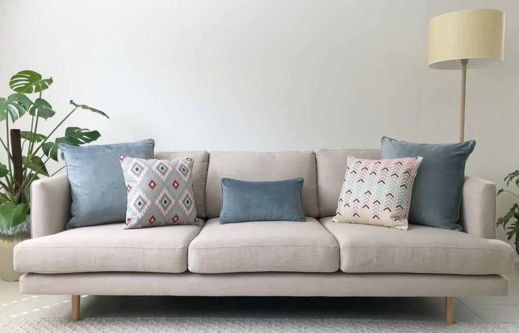 Neutral toned sofa decorated with patterned and velvet cushions in different pastel colours.