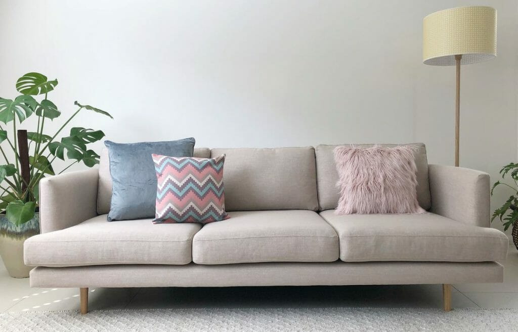Velvet, fur and chevron patterned cushions in pastel colours, on a neutral coloured sofa.
