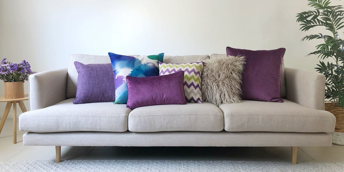 A gret sofa with purple and blue cushions in all different shapes and sizes