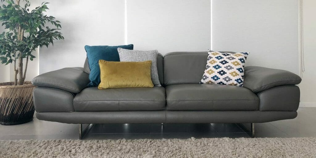 An arrangement of 3 in 1 cushions in mustard,blue and grey and a patterned cushions softens the appearance of the grey leather sofa.