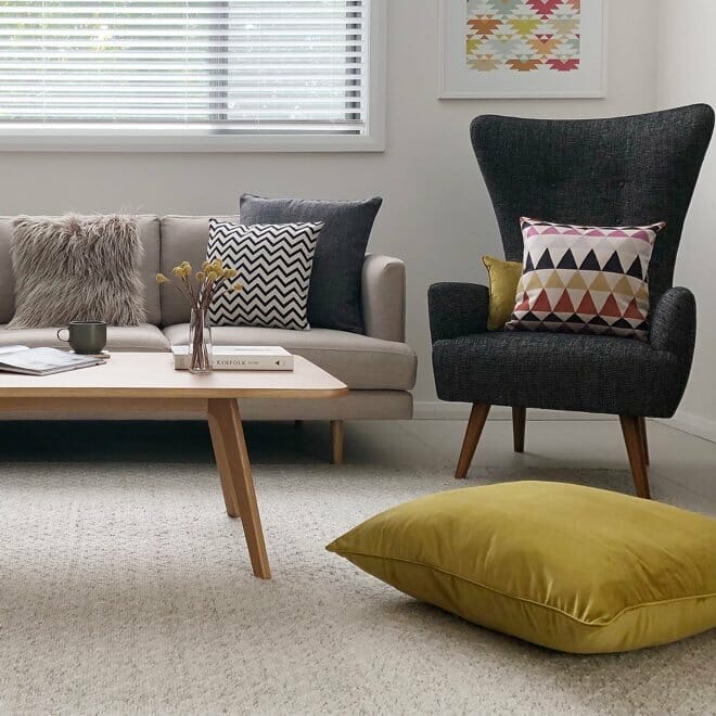 A highback chair decorated with a patterned cushion with a couple of block coloured cushions to achieve a vintage contemporary look.