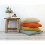 Stack of mustard, terracotta, neutral and sage coloured cushions against a white wall