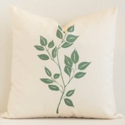 Cream botanical cushion leans elegantly against a brick wall. It has been crafted from a high quality outdoor material and has a square shape.