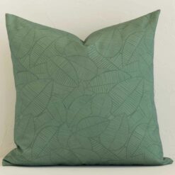 A large outdoor cushion in a delightful palm green tone rests against a white wall. The outdoor material appears to be of exceptional quality.