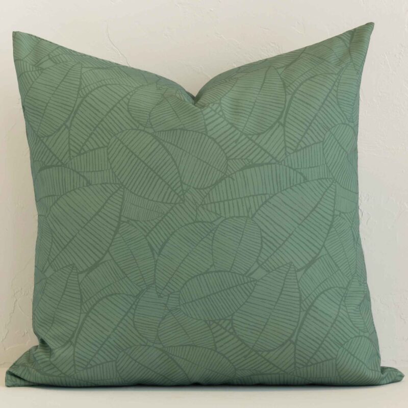 A large outdoor cushion in a delightful palm green tone rests against a white wall. The outdoor material appears to be of exceptional quality.
