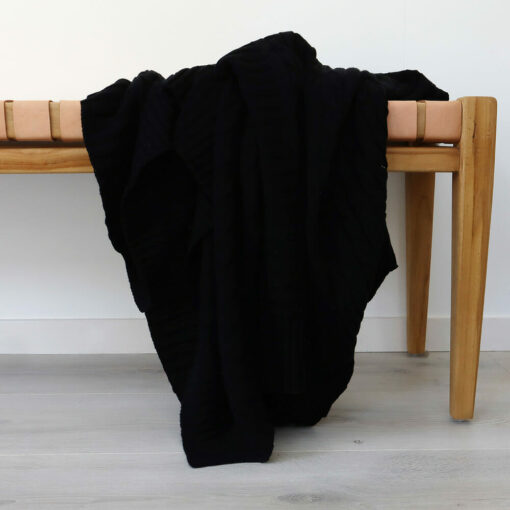An image of a black knitted throw draped over a stool