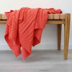An image of a coral knitted throw draped over a stool