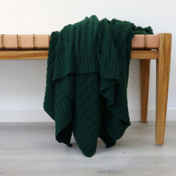 An image of a emerald green knitted throw draped over a stool.