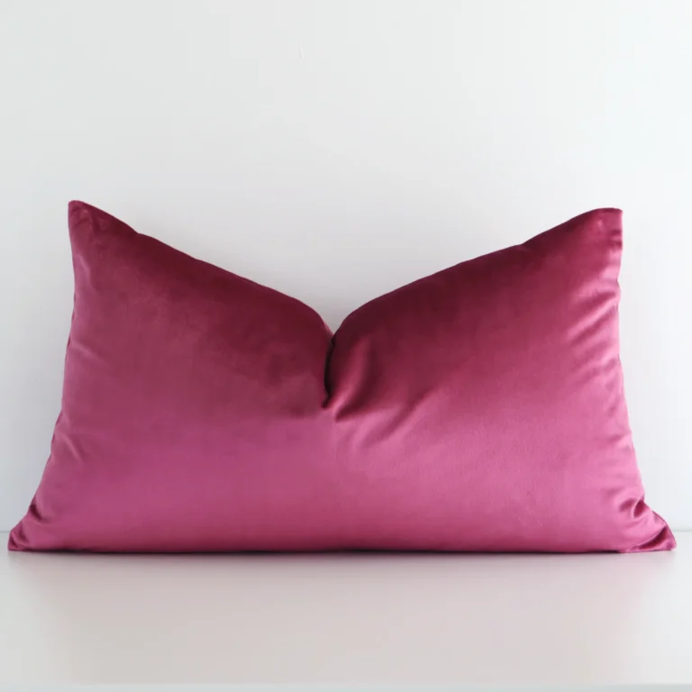 A pretty solid colour velvet cushion cover is shown against a white wall. It features a rectangle shape and a blush colour finish.