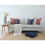 Light coloured sofa with, woven rug, wooden table, off-white throw and coral and navy cushions with floral prints
