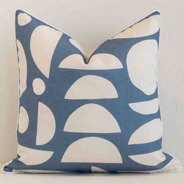 Bold square blue cushion positioned in front of white brickwork. Its geometric style pops on the outdoor fabric.