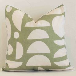 An attractive geometric outdoor cushion in front of a white brick wall. It has a square shape and is sage in colour.