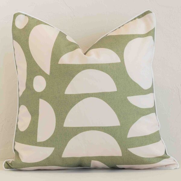 An attractive geometric outdoor cushion in front of a white brick wall. It has a square shape and is sage in colour.