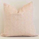 White wall with a stripe rust cushion laying against it. It has a distinctive outdoor fabric and has a square shape.