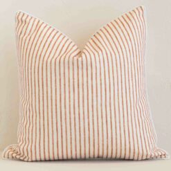 White wall with a stripe rust cushion laying against it. It has a distinctive outdoor fabric and has a square shape.