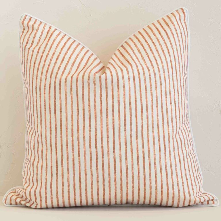 White wall with a stripe rust cushion laying against it. It has a distinctive outdoor fabric and has a square shape.