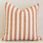 Square stripe cushion cover in cream and rust colour sitting upright in front of a brick wall. It has been made from a quality outdoor material.
