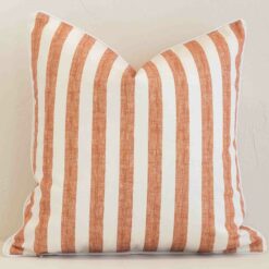 Square stripe cushion cover in cream and rust colour sitting upright in front of a brick wall. It has been made from a quality outdoor material.