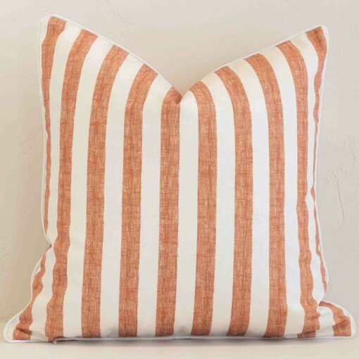 Square stripe cushion cover in cream and rust colour sitting upright in front of a brick wall. It has been made from a quality outdoor material.