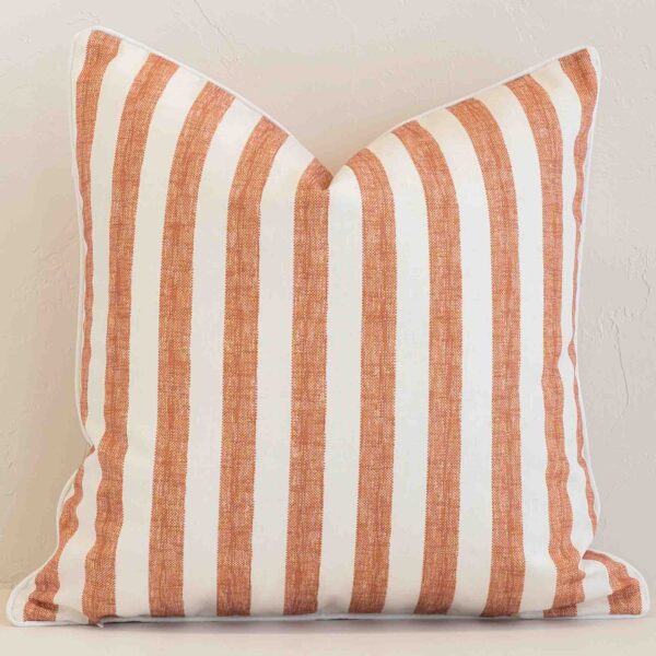 Square stripe cushion cover in cream and rust colour sitting upright in front of a brick wall. It has been made from a quality outdoor material.