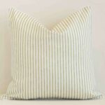 Outdoor square cushion with a stripe design in an upright position against a white brick wall. It is sage in colour.