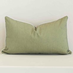Sage solid-colour cushion positioned in front of a brick wall. It has rectangle dimensions and is made from an outdoor material.