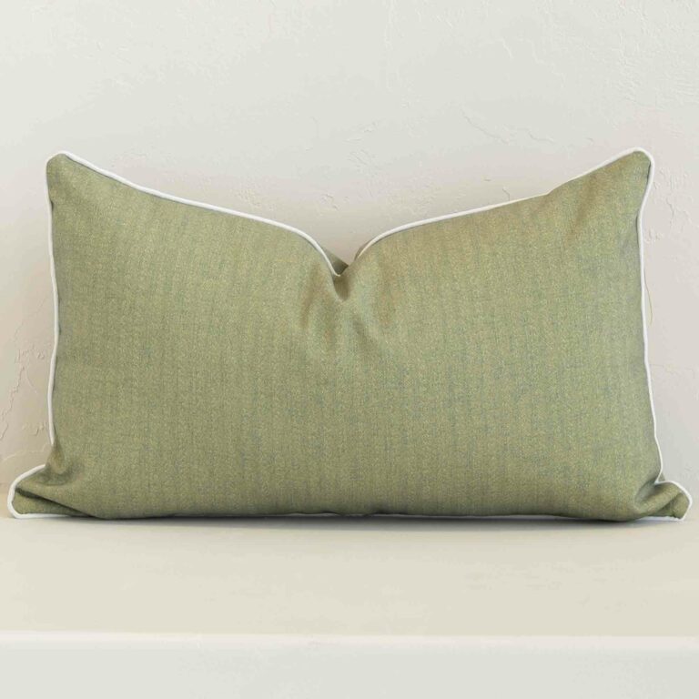 Sage solid-colour cushion positioned in front of a brick wall. It has rectangle dimensions and is made from an outdoor material.