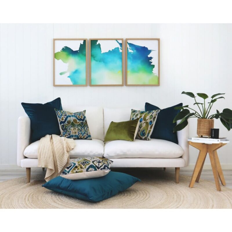 Olive and teal cushions and wall art in Ikat pattern against a white wall and sofa.
