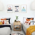 Kids bedroom with car kids cushions on twin beds with a throw blanket. On the wall are three kids wall prints that match the cushions