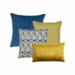 One blue square cushion, one yellow square cushion, one blue and yellow chevron design cushion and a gold velvet rectangular cushion in a set of four.