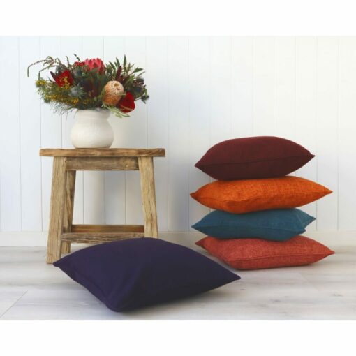 A stack of dark-colored cushions against a stool and white wall.