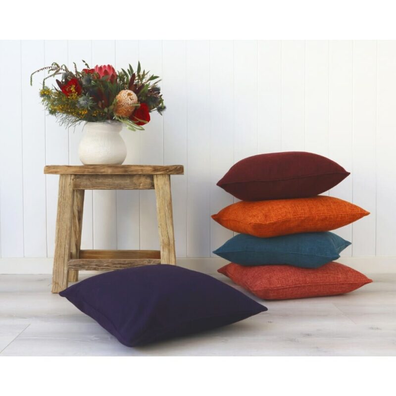 A stack of dark-colored cushions against a stool and white wall.