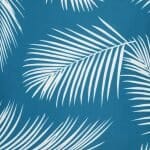 Close up view of a water resistant teal outdoor cushion cover that has a beautiful palm tree leaf print.