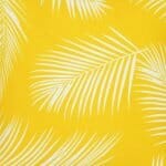 A close up view of a water resistant yellow outdoor cushion cover that has a beautiful palm tree leaf print.