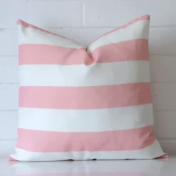 Pink cushion cover in front of a white wall. It has a large size and is made from an outdoor material.