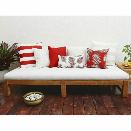 Red outdoor cushion covers in stripe, diamond and leaf patterns on top of wooden daybed.