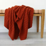 An image of rust coloured knitted throw draped over a stool.