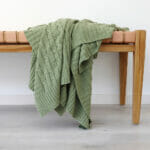 An image of a sage green knitted throw draped over a stool