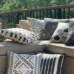 An outdoor setting is shown with a bold collection of black and white outdoor cushions adorning an outdoor sofa. The covers have striped and other markings which provide a tribal aesthetic.
