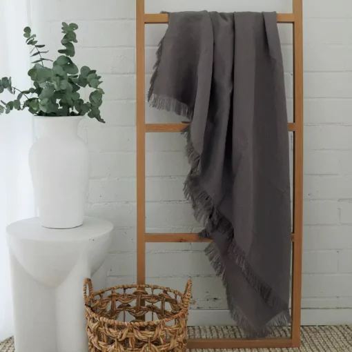 A wooden rack leaning against a white brick wall with a grey linen throw hanging on it.