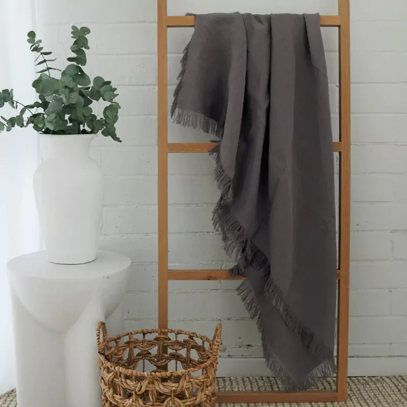 Sofia Grey Linen Throw - TH810 A wooden rack leaning against a white brick wall with a grey linen throw hanging on it.