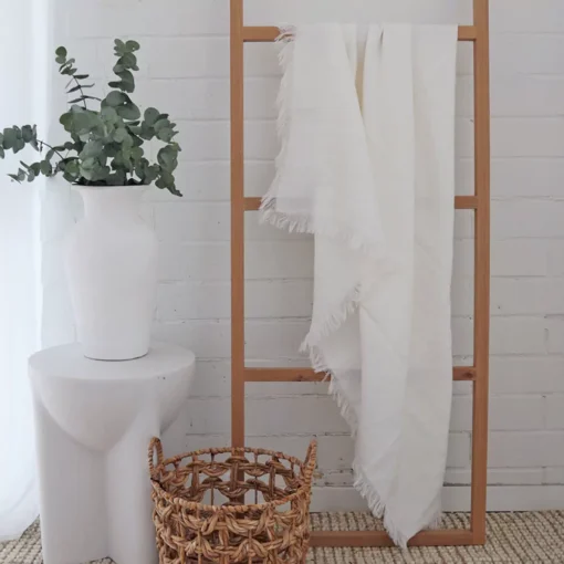 A soft white linen throw hangs on a stylish wooden rack.