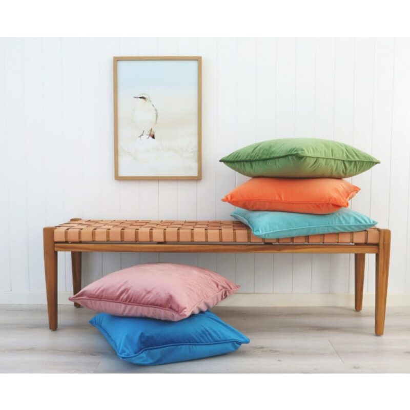 Colourful velvet cushion covers on wooden seat against a wall art
