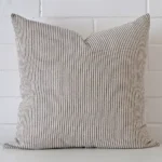 Striped cushion positioned in front of a brick wall. It has large dimensions and is made from a designer material.