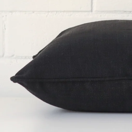 Square cushion in black colour laying flat. The viewpoint highlights the seams of the linen fabric