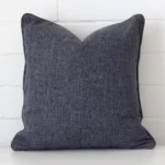 Here a charcoal linen cushion is shown styled against a white wall. It has a square design.